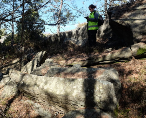 Jonna står och mäter in del av ett stenbrott. Inom lämningen, belägen i utredningsområdets nordvästra del, förekommer skrotsten samt märke efter rundkil. Flera stenbrott förekommer i närområdet. Foto mot norr.